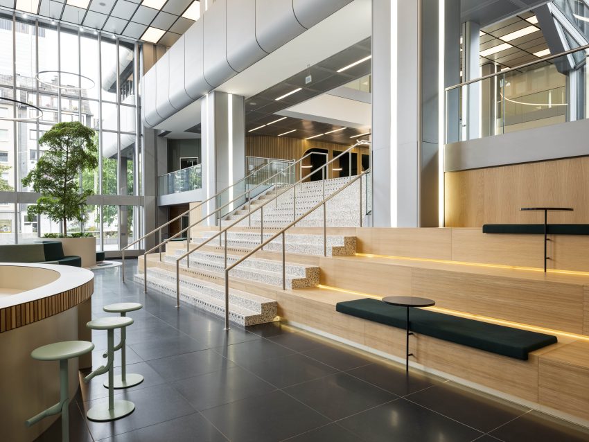 Modern interior with large windows, staircase with handrails, wooden seating elements and green stools