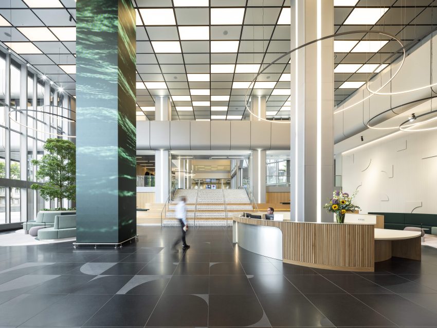 Bright reception hall with large staircase, round lights, seating areas and a reception desk with a bouquet of flowers